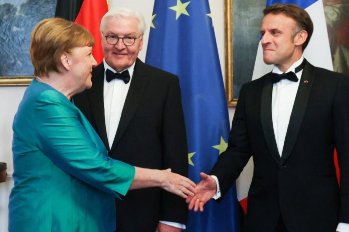 Nachdem sie Bundespräsident Frank-Walter Steinmeier begrüßt hatte, schüttelte Angela Merkel Emmanuel Macron herzlich die Hand. / Source: imago/Bestimage